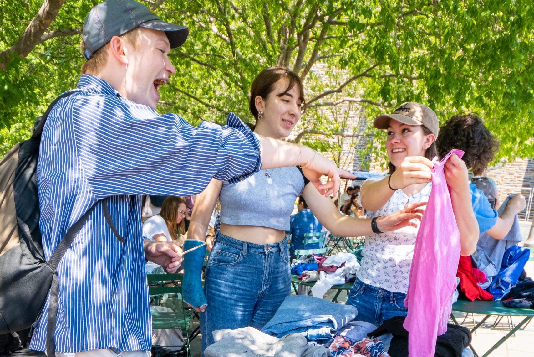 Three students examine a pink garment while standing over a table of folded thrifted clothes.