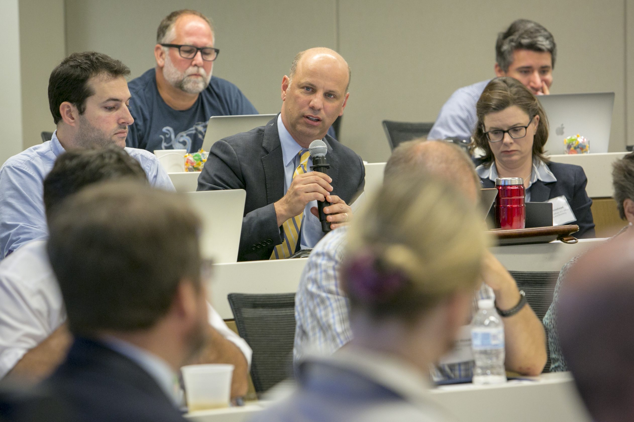 Sanford School of Public Policy Associate Professor of the Practice Tim Profeta holds a handheld microphone and speaks while sitting in an audience at an event.