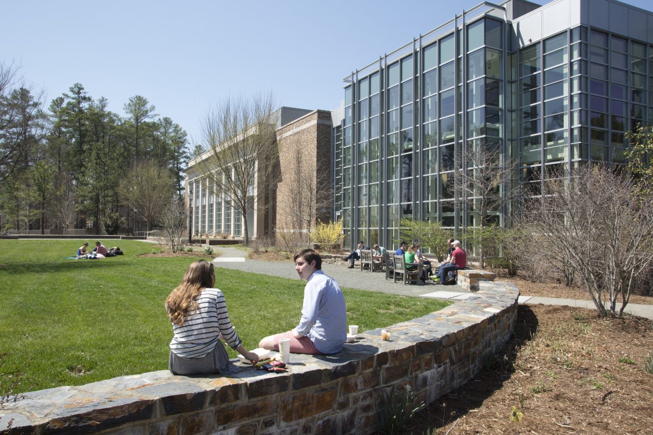 Students sitting outside on the stone wall outside of Duke's Law School.