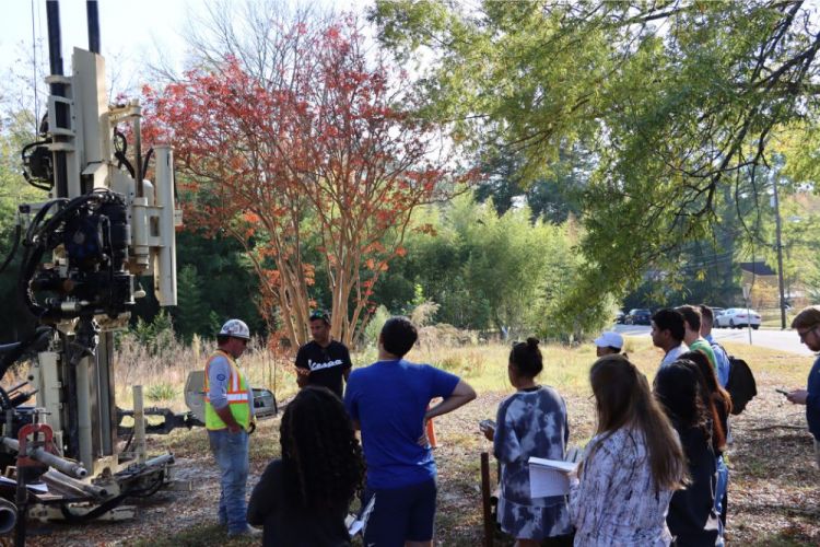 Brian McAdoo speaking with his students and drill operator at the geothermal dig site.