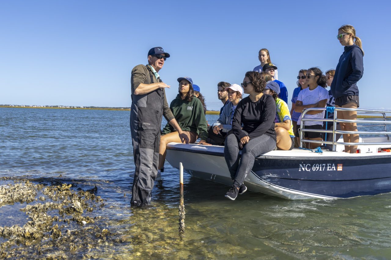 A Marine Lab faculty member speaking to a group of 13 students on a boat.