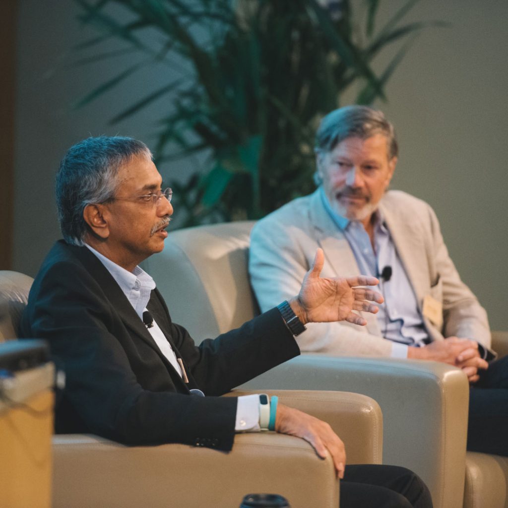 Two men sitting in chairs speaking on a stage