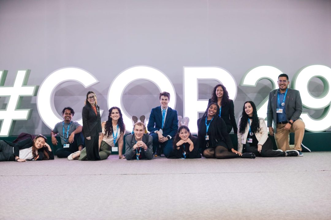 Students sitting and posing in front of COP29 giant sign