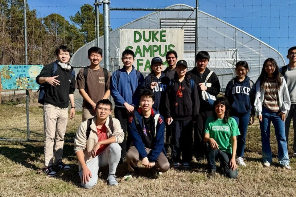 Students from Chinese language course at Duke Campus Farm in front of sign