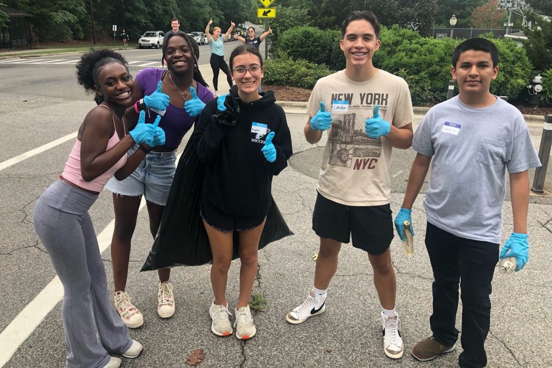 Five students on a street wearing gloves helping to clean up litter.